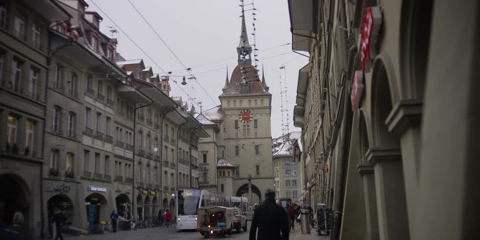 A cable car and pedestrians move through the city of Bern, Switzerland with the Kafigturm tower in the background