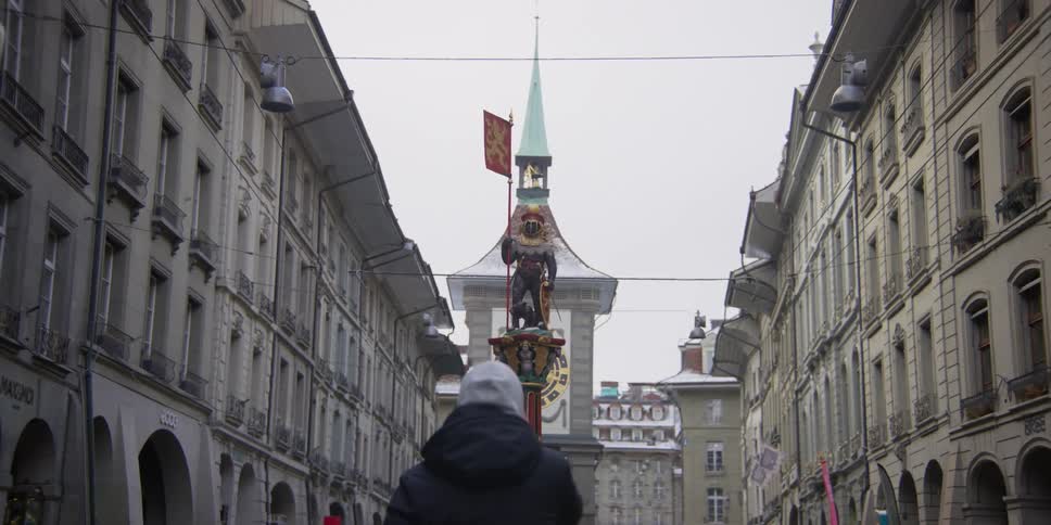 Person stands looking at the Zahringerbrunnen bear statue and the Zytglogge Tower in Bern, Switzerland