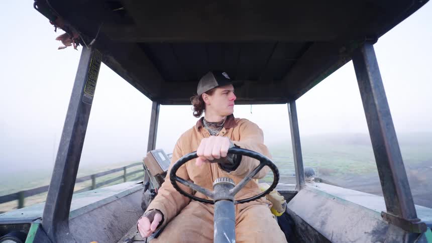 Man driving a farm tractor in a foggy pasture