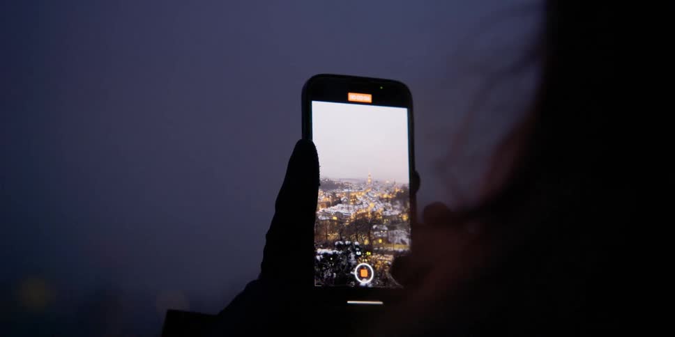 A woman films the nighttime city skyline of Bern, Switzerland on her smartphone