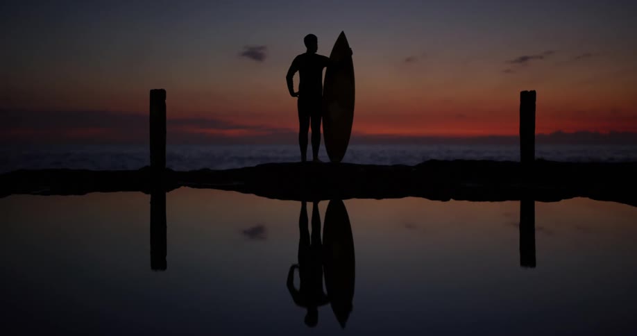 A surfer holds his board on the beach