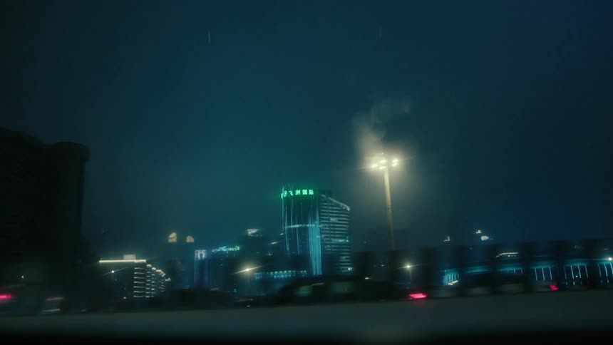 View from the window of a vehicle moving through the streets with modern buildings in a metropolis at night and in rain