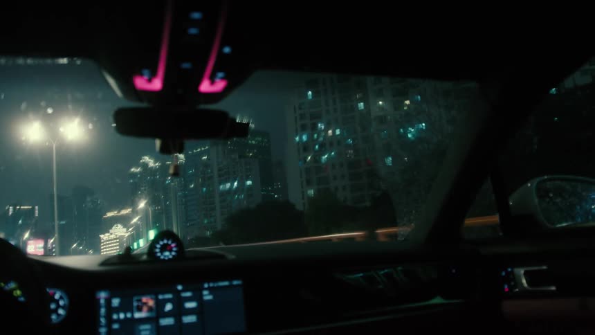 Windshield wipers move across the windshield as car drives through the city at night