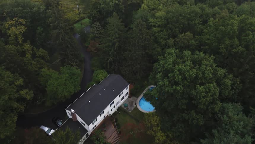 Aerial of a large white house surrounded by a forest on a summer day