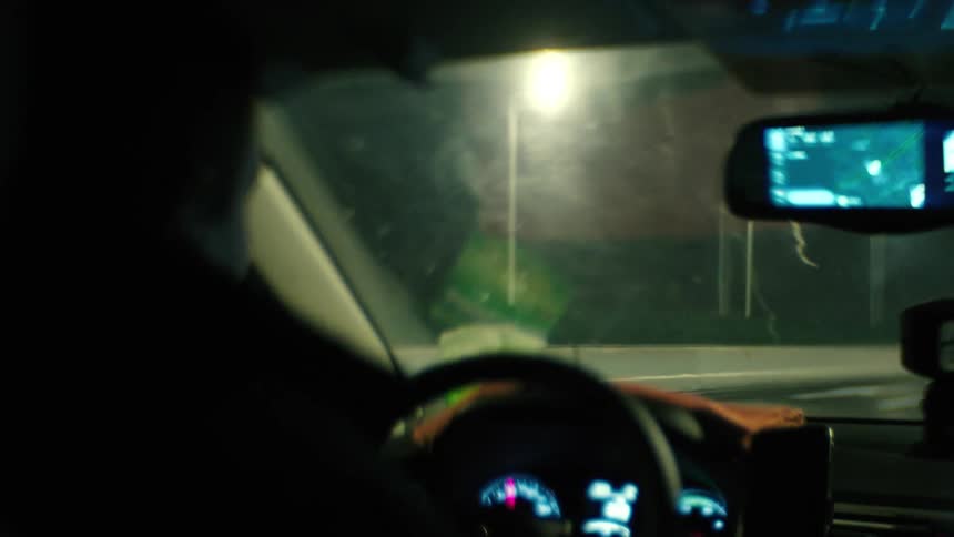 Silhouette of the side face of a man driving a vehicle through the streets of a city at night