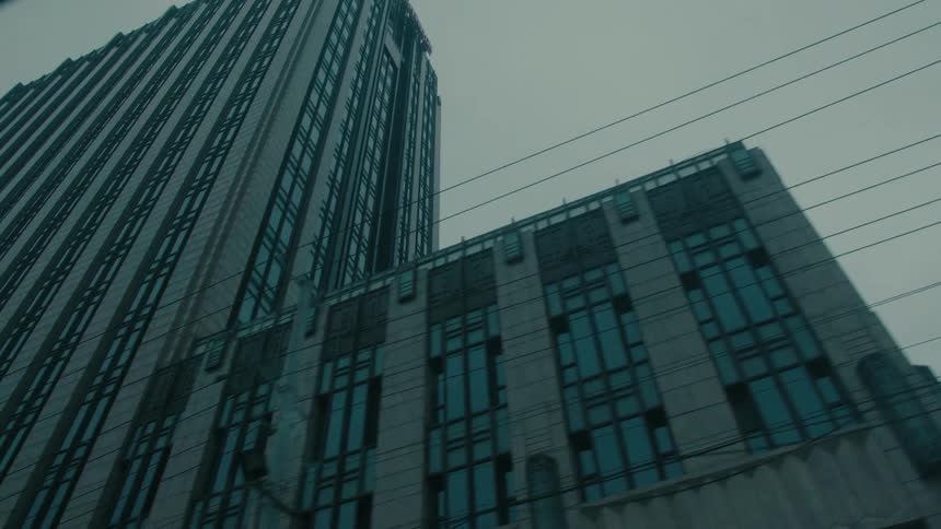 View from the window of a moving vehicle to large buildings in a metropolis on a cloudy day