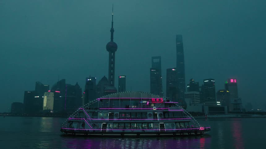 Panorama of a metropolis with skyscrapers and modern buildings illuminated at night and the seaside with a tourist boat passing by