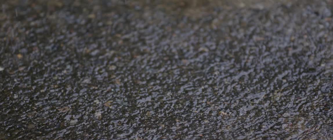 Closeup of the ground with rain falling and forming puddles of water in slow motion