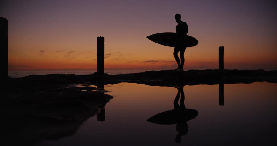 Silhouette of a surfer walking next to a beach at sunset
