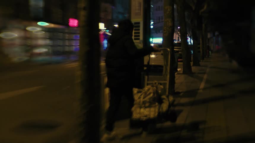 Urban city street at night with a person checking and scavenging through trash