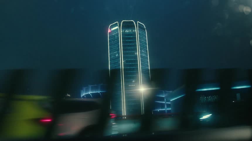 Driving by a stadium and a tower building both decorated with bright lights
