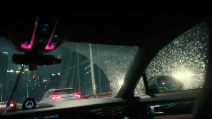 Inside view of the windshield of a car traveling through the streets of a metropolis on a rainy day at night