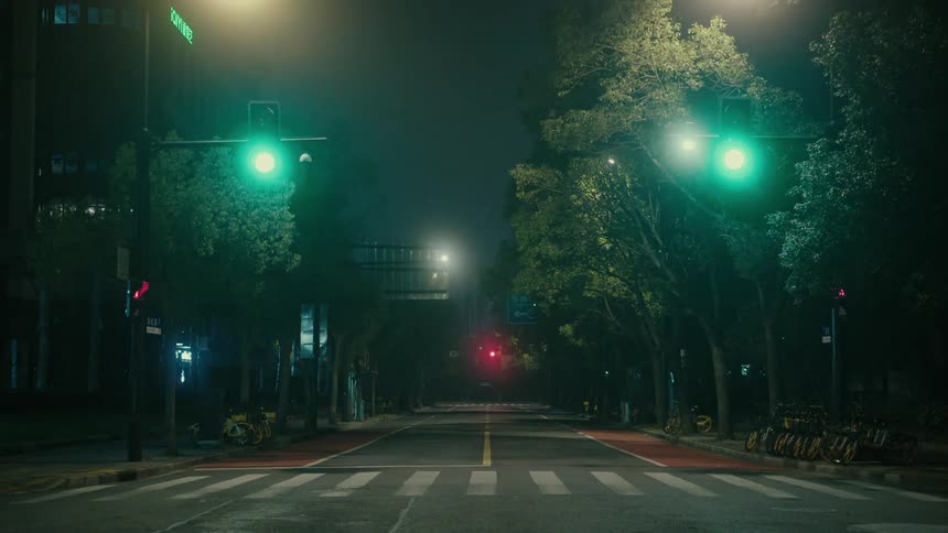 A deserted city street at night illuminated by streetlights and traffic lights