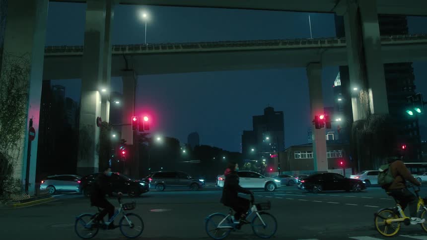 Panorama of a street with vehicle traffic and pedestrians riding bicycles at night and the silhouette of skyscrapers on the horizon