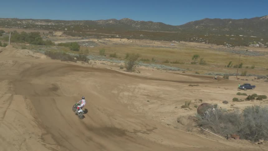 A person rides a dirt bike on a dirt track outside