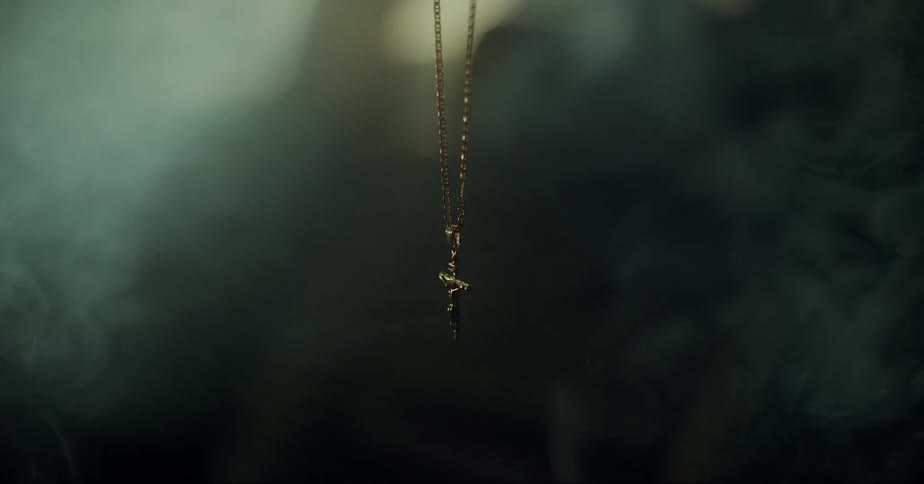 Pale vapor flows through the air around a hanging crucifix necklace
