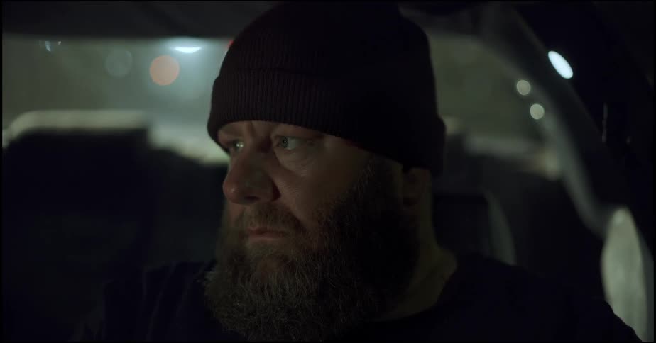 Man with facial hair wearing black beanie sits inside vehicle