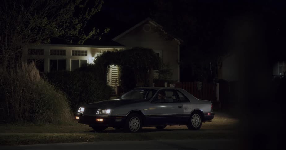 Man inside car parked next to a house at night