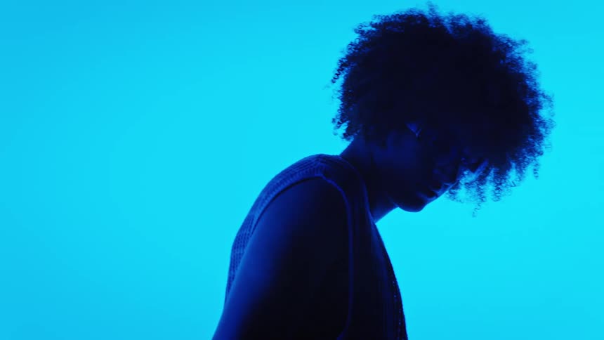 Side portrait of a model in fashionable clothes running her hand through her hair in a studio with vibrant blue lighting