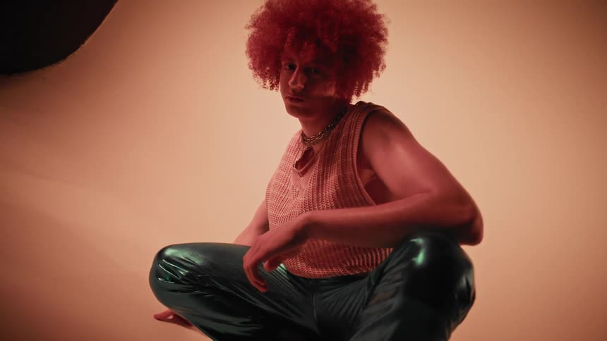 Curlyhaired model man crouching on the floor of a studio with warm lighting
