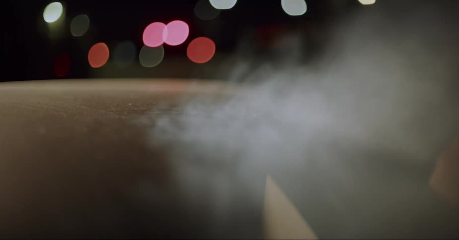 Vapor flows from top of door as man opens car at night and exits the vehicle