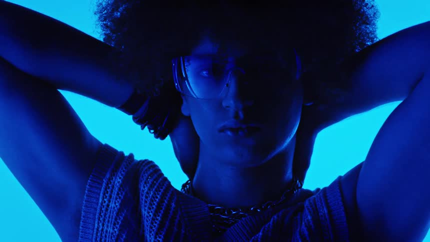 Portrait of a curlyhaired model posing in a studio environment with electric blue lighting