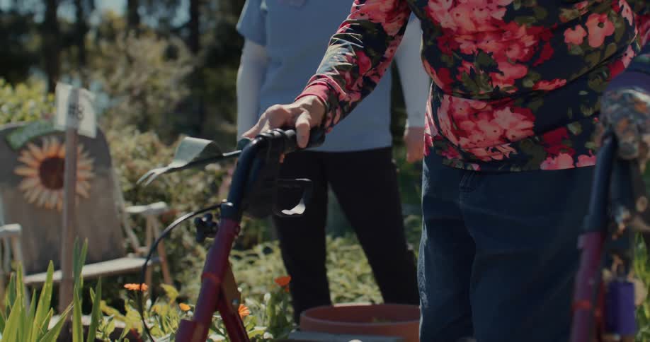 Hands of an elderly lady with the help of a mobile chair and holding a rake while walking in a garden