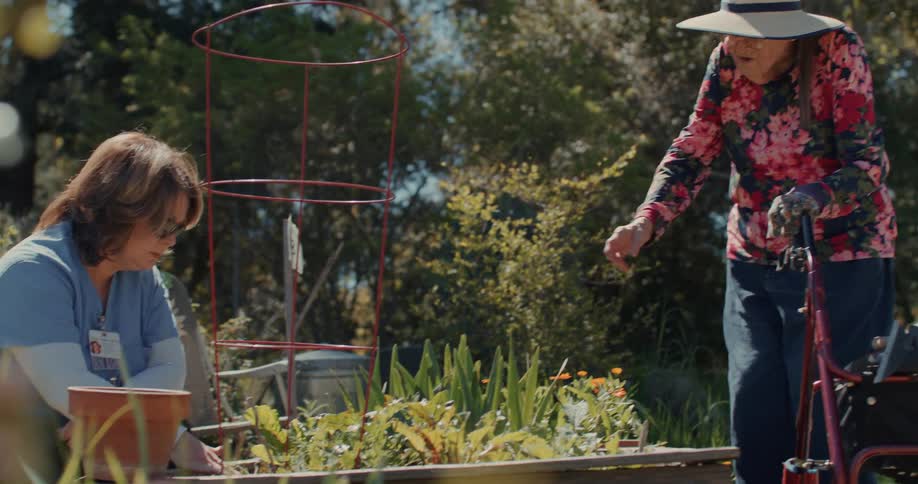 A nurse helps an elderly woman to tend a garden