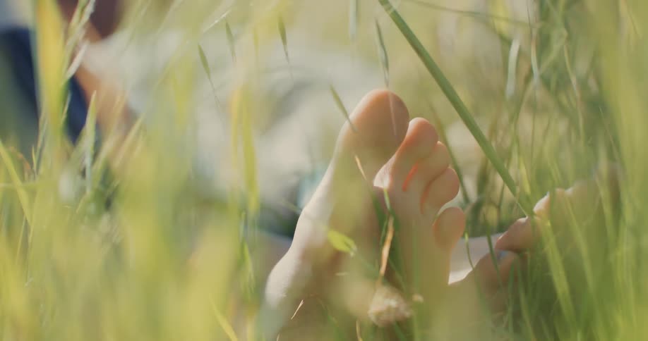 Feet of a woman lying on natural grass with sunlight reflection