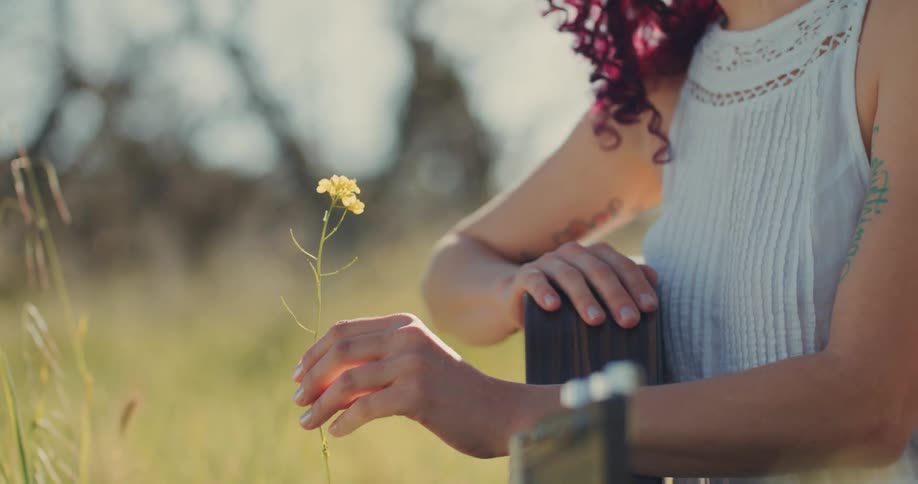 A woman is holding a flower on the field