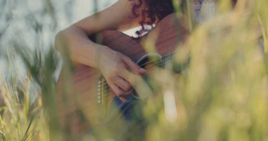 Hands of a woman sitting in a field playing the guitar