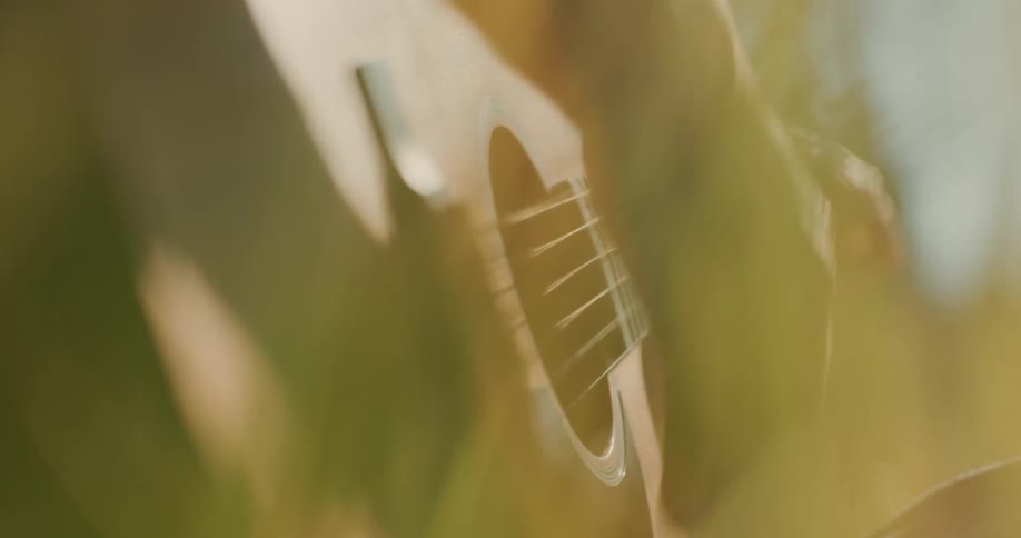 A person sitting outside strums on an acoustic guitar with their fingers
