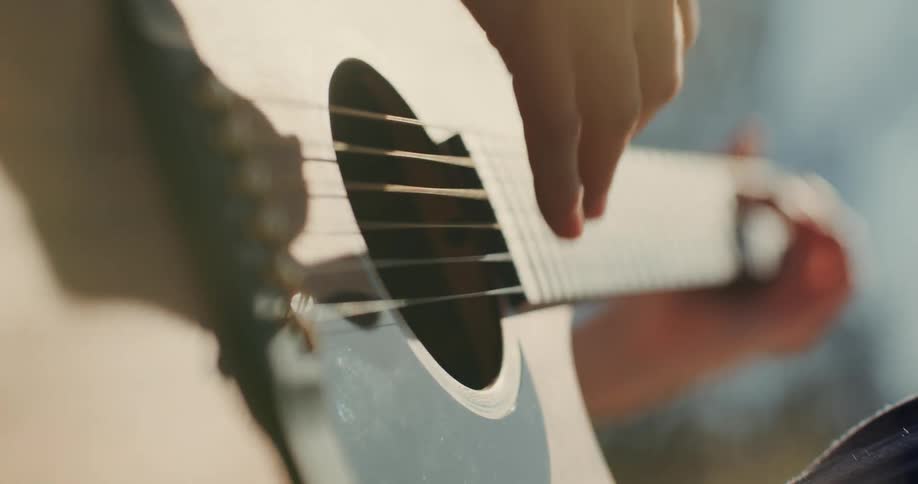Musician moves their fingers on the fretboard as they strum the guitar strings