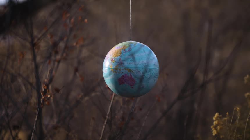 World globe of earth sways as it hangs on a string and spins outside among plants