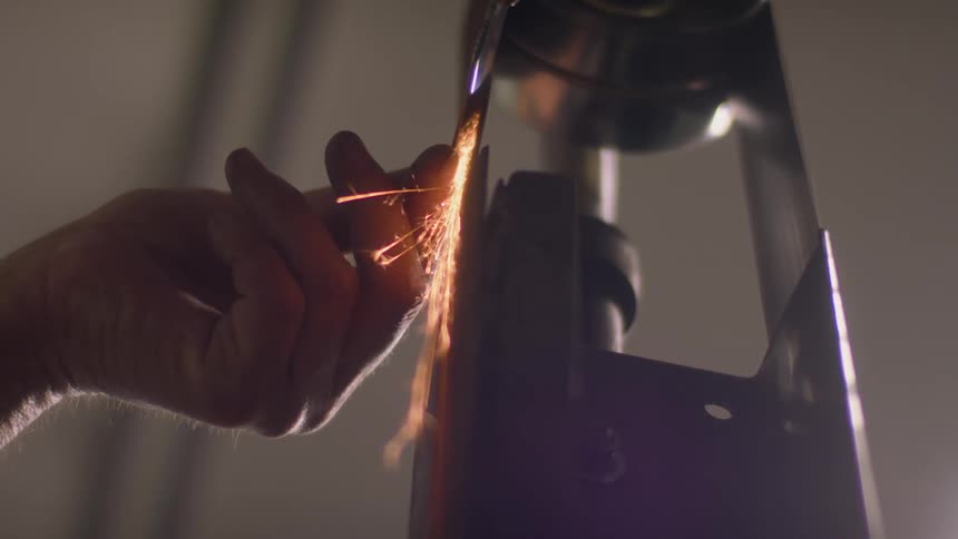A person uses a machine to smooth a piece of metal which creates many sparks