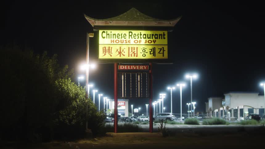 A sign for a chinese restaurant and a parking lot filled with cars