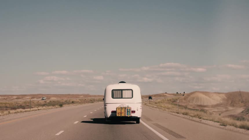 A camper drives down a road in a desert