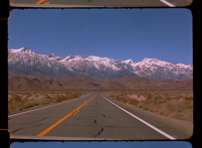 Point of view from the windshield of a vehicle going down a straight street and snowcovered mountains in the background on the horizon