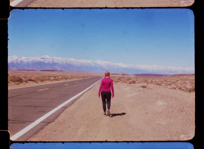 Woman walking on the side of a road through the desert caught on vintage film