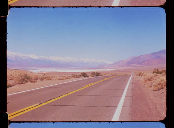 Panorama of a long paved road with desert vegetation around it and mountains on the horizon