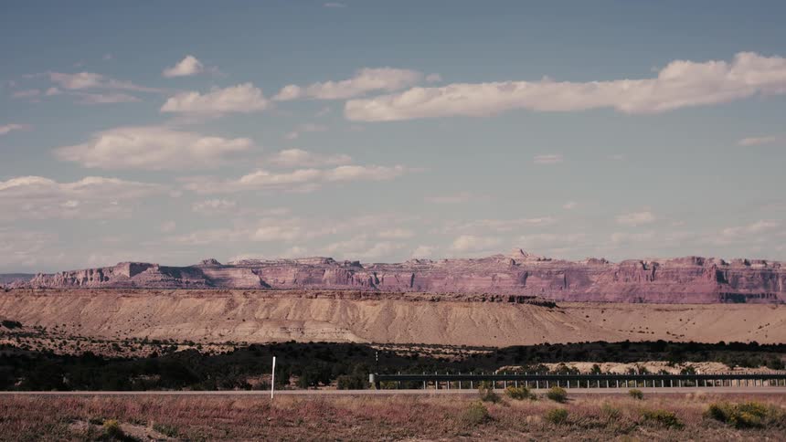 A truck on the highway drives past the badlands