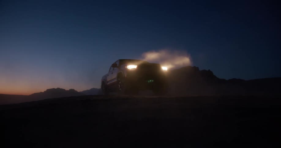 A pickup truck turns on the headlights on a dusty night in the desert