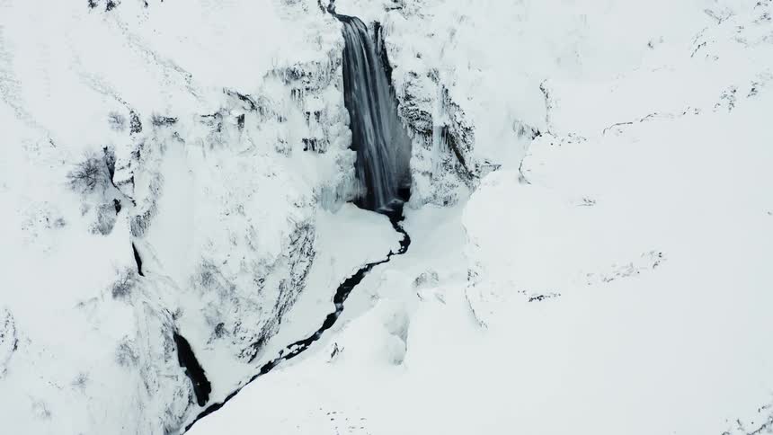 Aerial of a hidden waterfall flowing rapidly surrounded by snow covered mountains