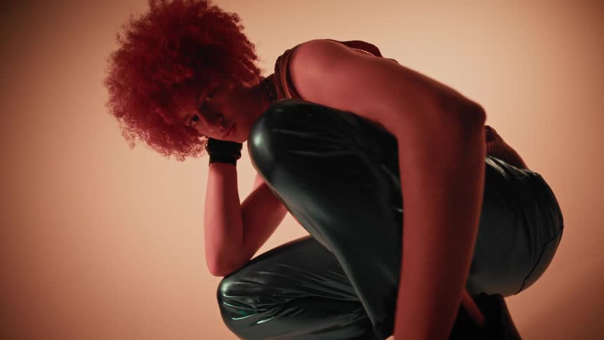 Young male model squatting in latex pants modeling in a studio with warm lighting