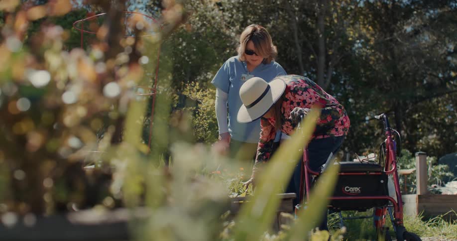 Nurse in a blue coat next to an elderly woman standing in a garden
