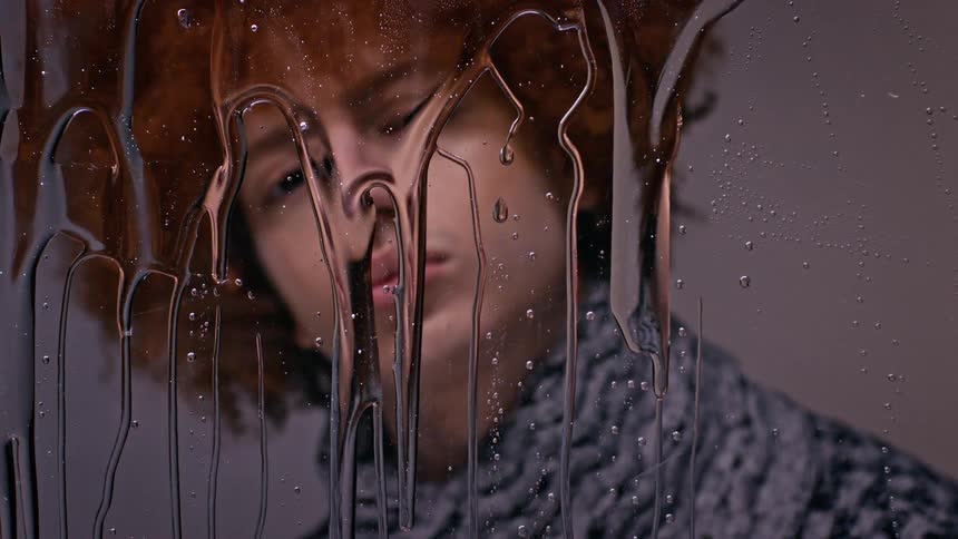 Portrait of a model man looking at himself in a mirror with transparent liquid falling