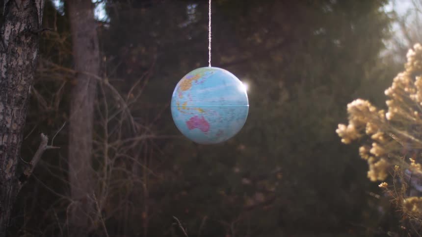 A small globe hanging from a string spins in the woods at morning