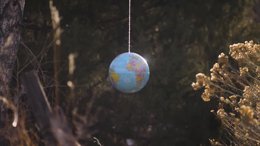 Scientific globe in orbit hanging by a white thread in a forest with sunlight reflection