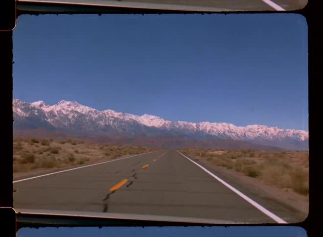 Point of view of a vehicle traveling on asphalt with desert nature around and mountains ahead with snow