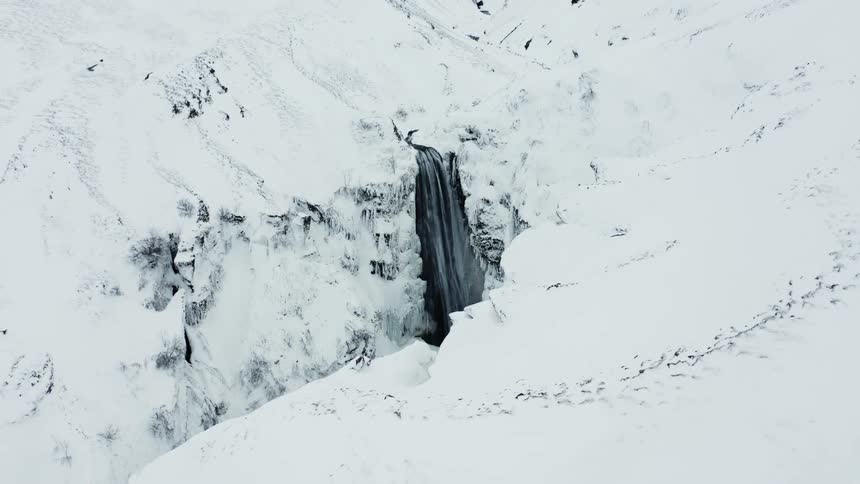 Aerial panorama of snowcapped white mountains and a waterfall with freefalling waters